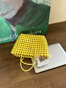 Dettaglio della borsa tote gialla intrecciata a rete con trama a quadretti su legno