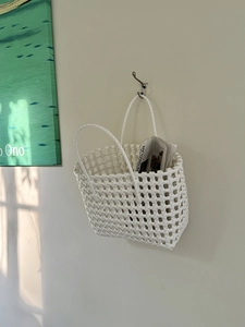 Dettaglio della borsa intrecciata bianca appesa al muro con giornali per un'atmosfera accogliente