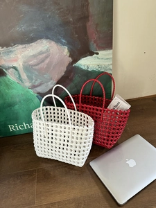 Dettaglio di borse tote intrecciate a mano in bianco e rosso su pavimento in legno