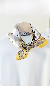 Detail of a floral silk scarf knotted on a white sweater with yellow and grey patterns