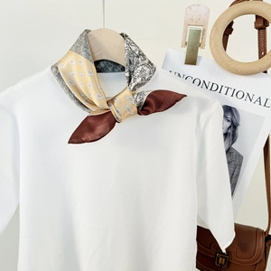 Elegant silk scarf with paisley and leaf patterns styled on a white knit shirt