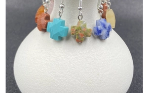 Detailed view of colorful natural stone cross earrings hanging on a white ceramic vase