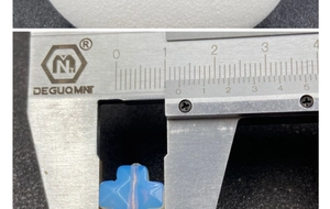 Macro detail of natural stone cross pendant being measured with calipers showing 10mm size
