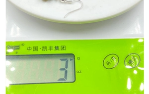 Detail showing the lightweight 3g green natural stone cross earring on a digital scale