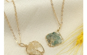 Close-up of heart and square crystal tree of life pendants on textured beige fabric