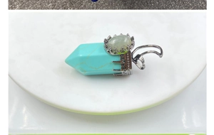 Macro view of blue turquoise hexagonal pendant with green gemstone and silver crown setting