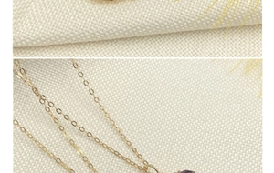Macro shot of gold cross chain and teardrop purple crystal pendant on linen