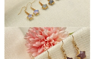 Macro detail of star-shaped crystal drop earrings with gold-plated trim on white canvas