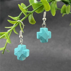 Natural turquoise cross dangle earrings with silver hooks hanging on green plants