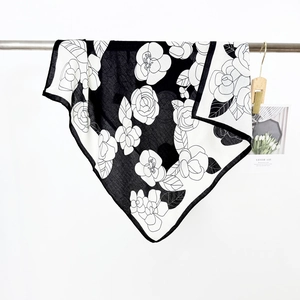 Elegant black and white camellia silk scarf hanging on a metal rack for women
