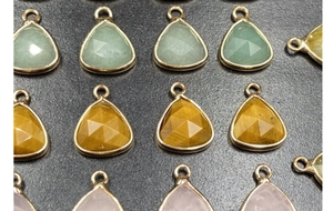 Macro detail of faceted teardrop charms with gold metal edging in multiple colors