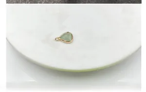 Macro shot of a teardrop light green stone pendant with a gold-plated metal border