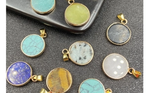 Close-up of assorted round semi-precious stone pendants with gold plated edges on black background
