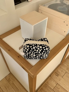 Detail of floral cosmetic bag with white daisy print and portable side handle on white desk