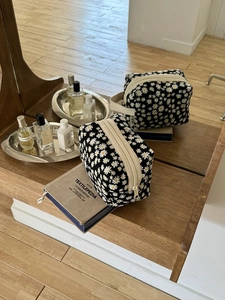 Detail of floral daisy toiletry bags with metal zippers on a wooden shelf