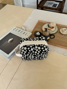 Detail of a black daisy floral cosmetic bag with white zippers on a wooden table setup