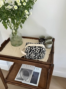 Close-up of black canvas cosmetic bag with small daisy pattern on a wooden shelf
