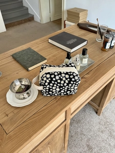 Detail of floral makeup bag with white daisies and a zipper handle on wooden desk