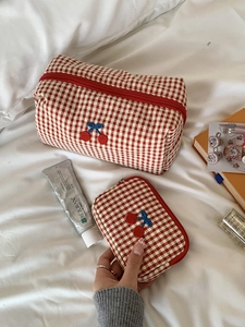 Detail of red checkered cosmetic bag featuring cherry embroidery and blue ribbon bows