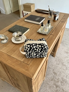 Detailed view of the daisy print makeup bag on a wooden table with lifestyle accessories