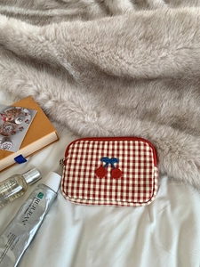 Red checkered makeup bag with embroidered cherries on a cozy fabric background