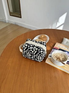 Detail of a black cosmetic bag with white daisy patterns on a warm wooden table