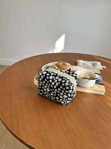 Close-up of a daisy pattern travel toiletry bag on a wooden table with soft lighting