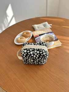 Close-up of black daisy pattern toiletry bag with zipper on a wooden table in sunlight