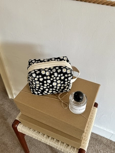 Detail of a black floral toiletry bag with white daisy prints on Kraft gift boxes