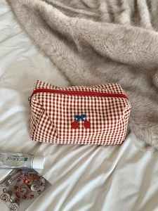 Close-up of red checkered makeup bag with cherry embroidery on a cozy blanket