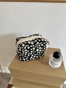 Detail of floral daisy toiletry bag with white zipper and handle on a kraft paper box