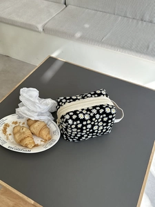 Close-up of black floral toiletry bag with daisy patterns and white zipper on a table