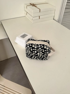 Close-up of portable daisy print cosmetic bag with white zipper and handle on a table
