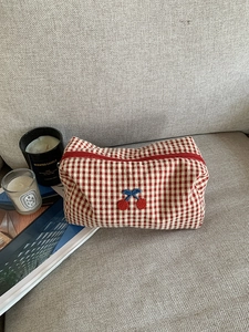 Detail of red checkered cosmetic bag featuring embroidered cherries on fabric texture