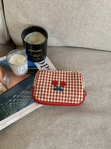 Detail of red checkered pouch with cherry embroidery on a cozy living room sofa
