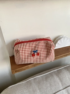 Close-up of red plaid makeup bag featuring 3D cherry embroidery and red zipper