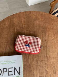Detail of red checkered cherry embroidery storage pouch on a vintage wooden table
