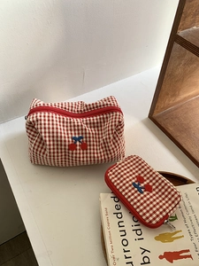 Detail of red gingham cherry embroidery cosmetic bags on a stylish wooden shelf