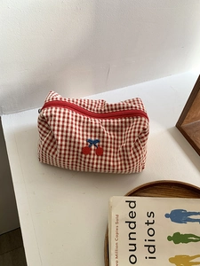 Red checkered canvas cherry makeup bag with bow embroidery on a minimalist wooden tray