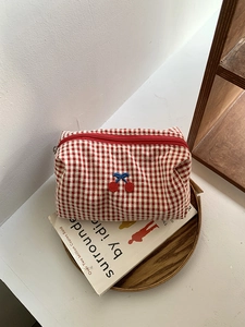 Detail of gingham makeup bag with cherry embroidery on a wooden tray with books
