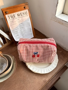 Detail of red checkered cherry cosmetic bag in a lifestyle setting on a ceramic plate