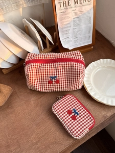 Detail of red checkered makeup bags with cherry embroidery on a rustic wooden table