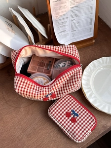 Detail of red checkered cosmetic bag featuring cherry embroidery and secure zipper