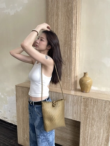 Close-up of golden woven shoulder bag with detailed texture and ball knot closure