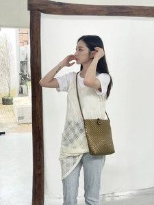 Detail of a woven bronze crossbody bag with round buckle shown on a model