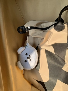 Detail of white plush puppy coin purse with zipper closure hanging on a beige bag