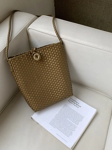 Detail of minimalist golden woven bucket bag texture with braided strap on white sofa