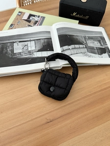 Dettaglio mini custodia trapuntata nera per auricolari su una scrivania in legno