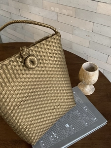 Detail of metallic gold woven tote bag with spherical closure on a wooden surface