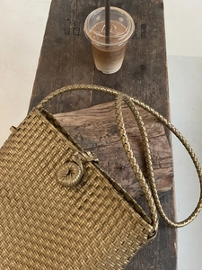 Detailed view of gold woven shoulder bag with metallic finish on a rustic wooden table